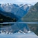 The Hardangerfjord in Norway with snow capped mountains in the distance and lush hillsides reflected in the calm water